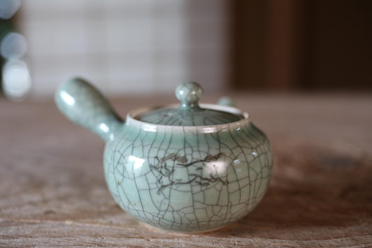 A ceramic teapot with a green and white color scheme and a decorative design on its surface, placed on a wooden surface.