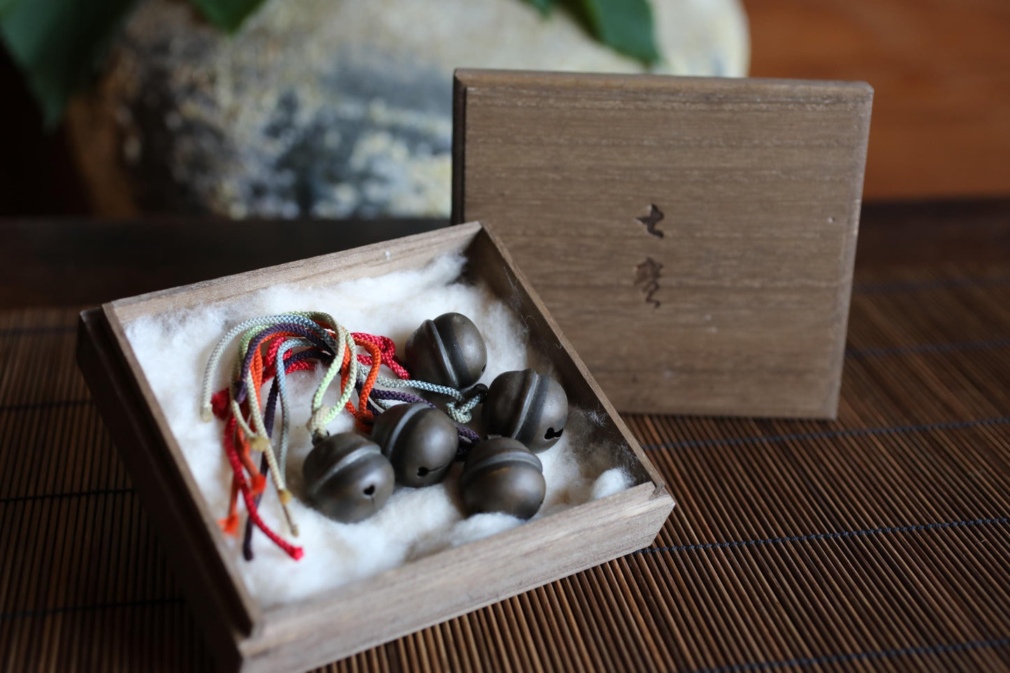 A wooden box containing several small, round bells, possibly made of metal, placed on a wooden surface.