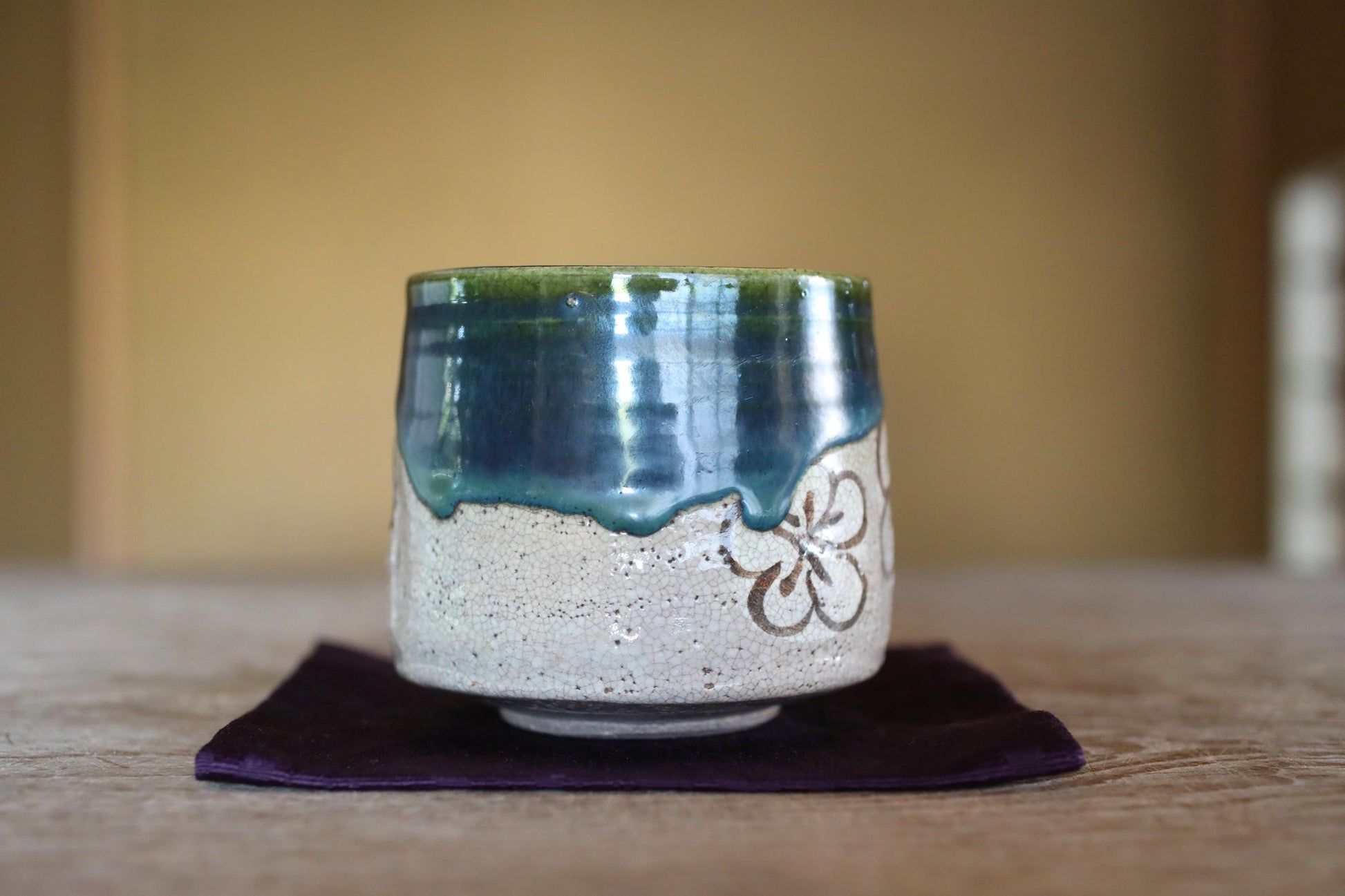 A ceramic mug with a blue and white design sits on a purple cloth on a wooden surface.
