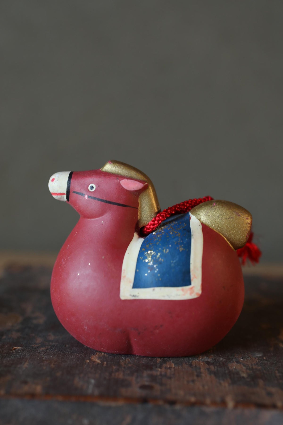 A red toy horse with a blue and gold design on its side is sitting on a wooden surface.