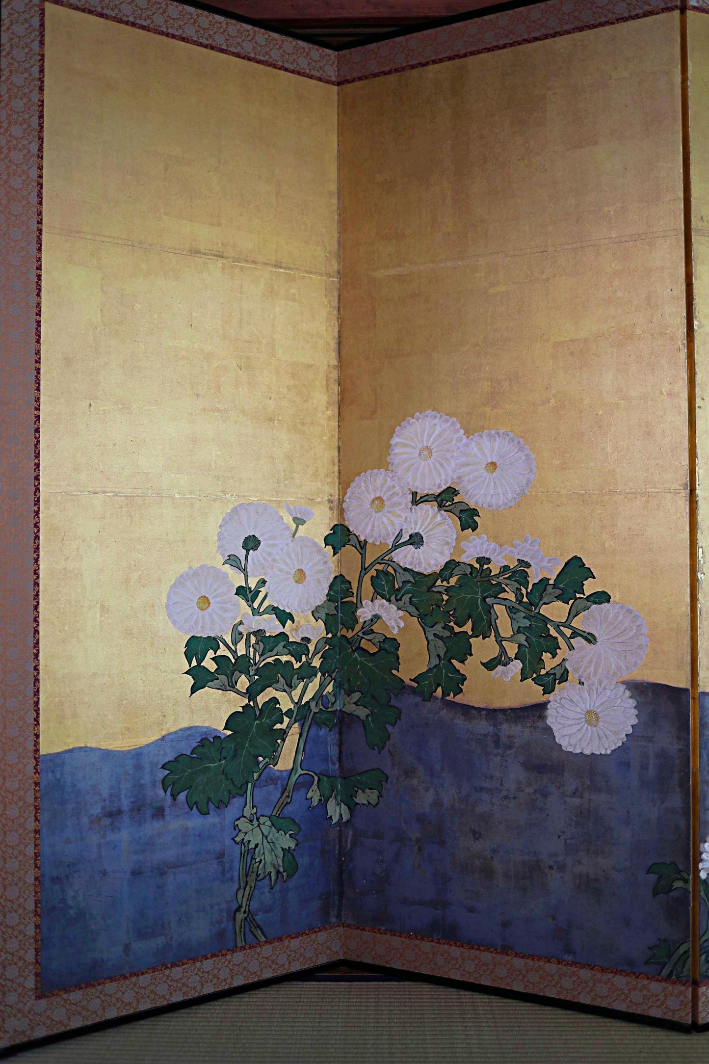 a large, intricately designed floral arrangement with white flowers and green leaves, set against a golden background.