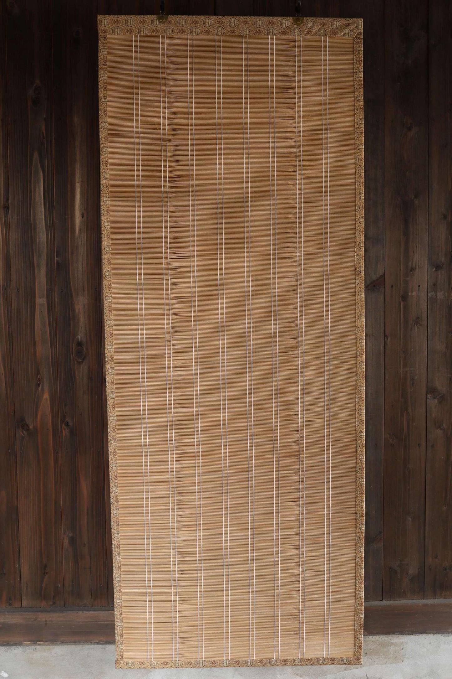 a bamboo screen or blind with vertical slats, placed against a wooden wall.