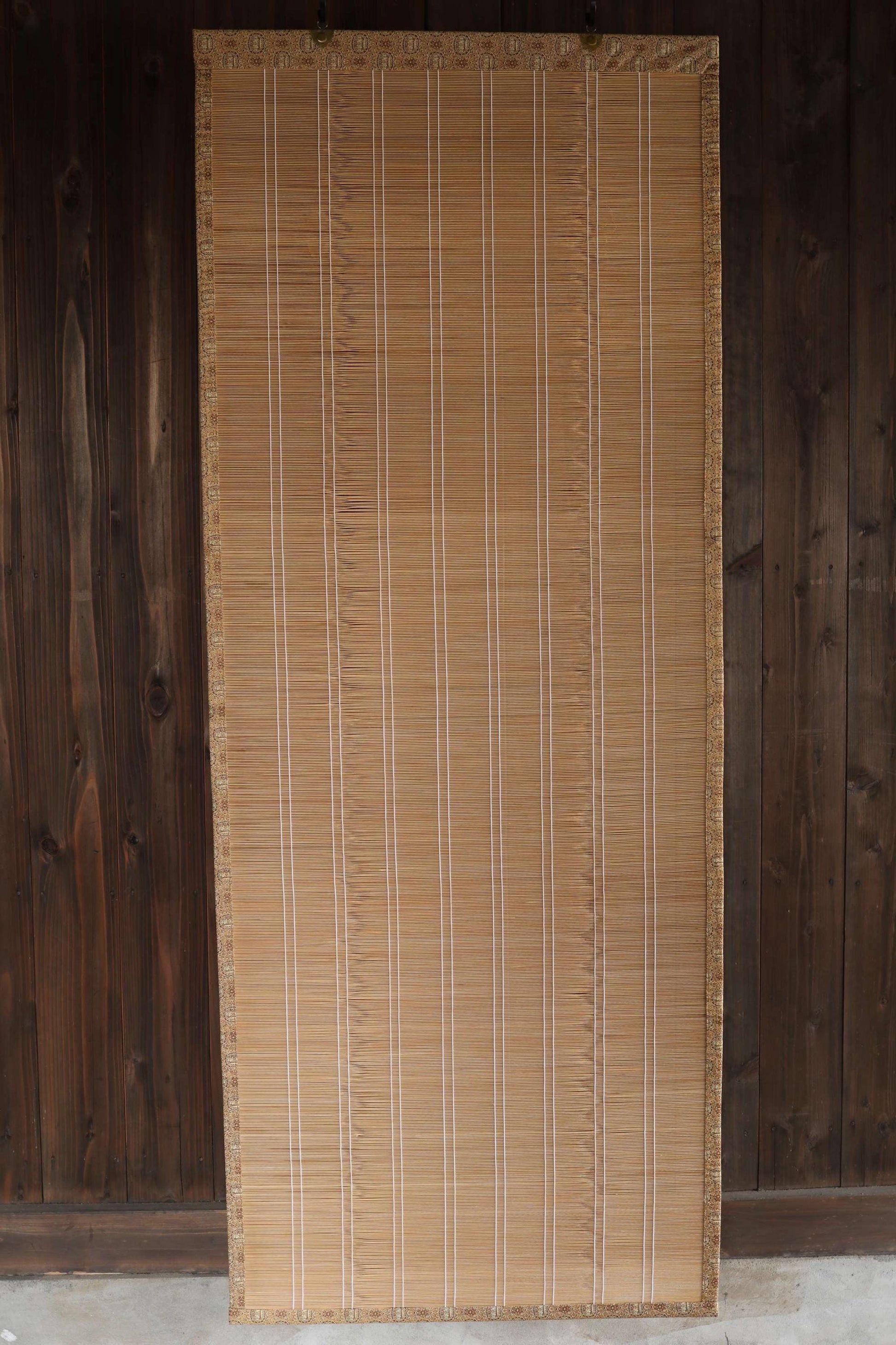 a bamboo screen or blind with vertical slats, placed against a wooden wall.