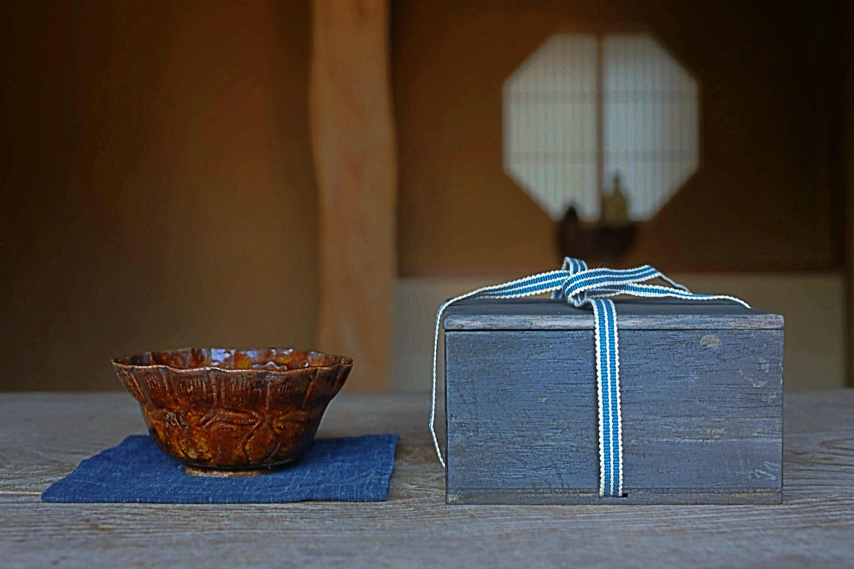 a wooden table with a brown bowl and a wooden box with a blue ribbon tied around it, placed on a blue cloth.