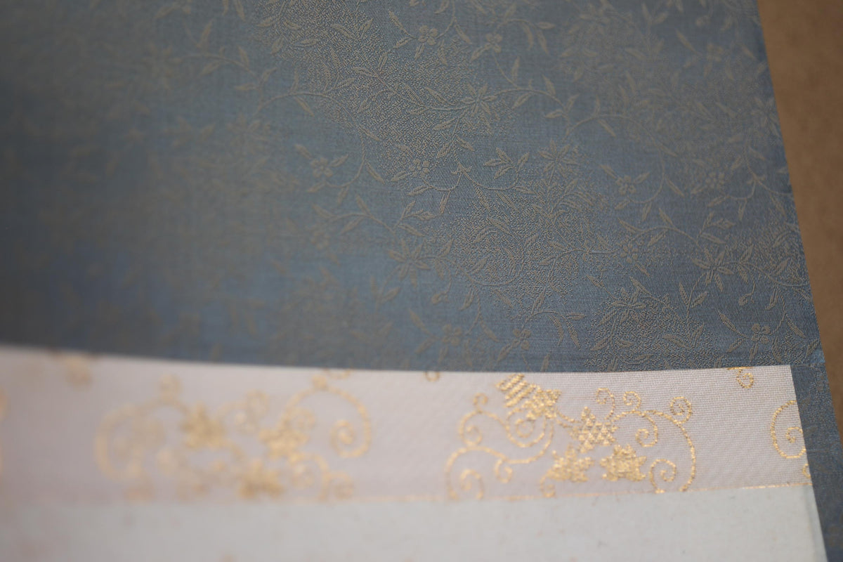 a close-up view of a blue fabric with a gold floral pattern.