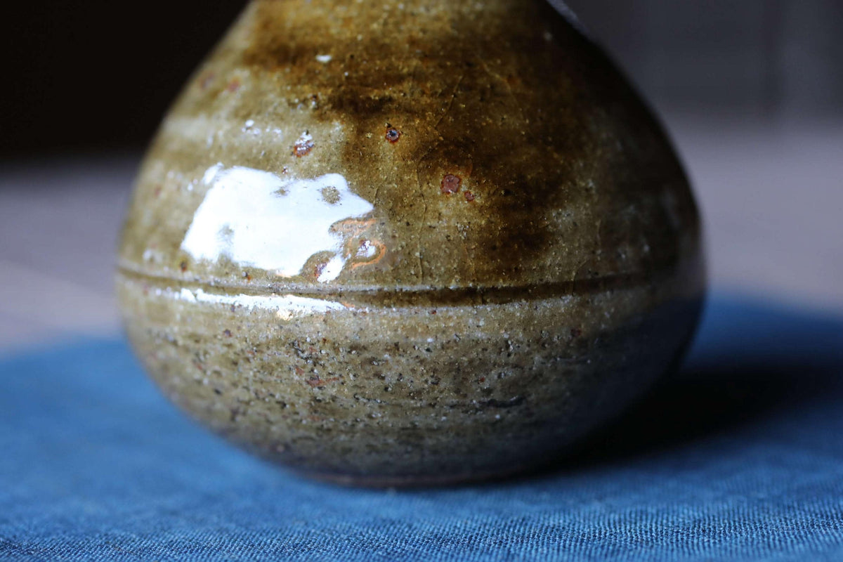 A close-up image of a brown ceramic vase with a textured surface, resting on a blue fabric background.