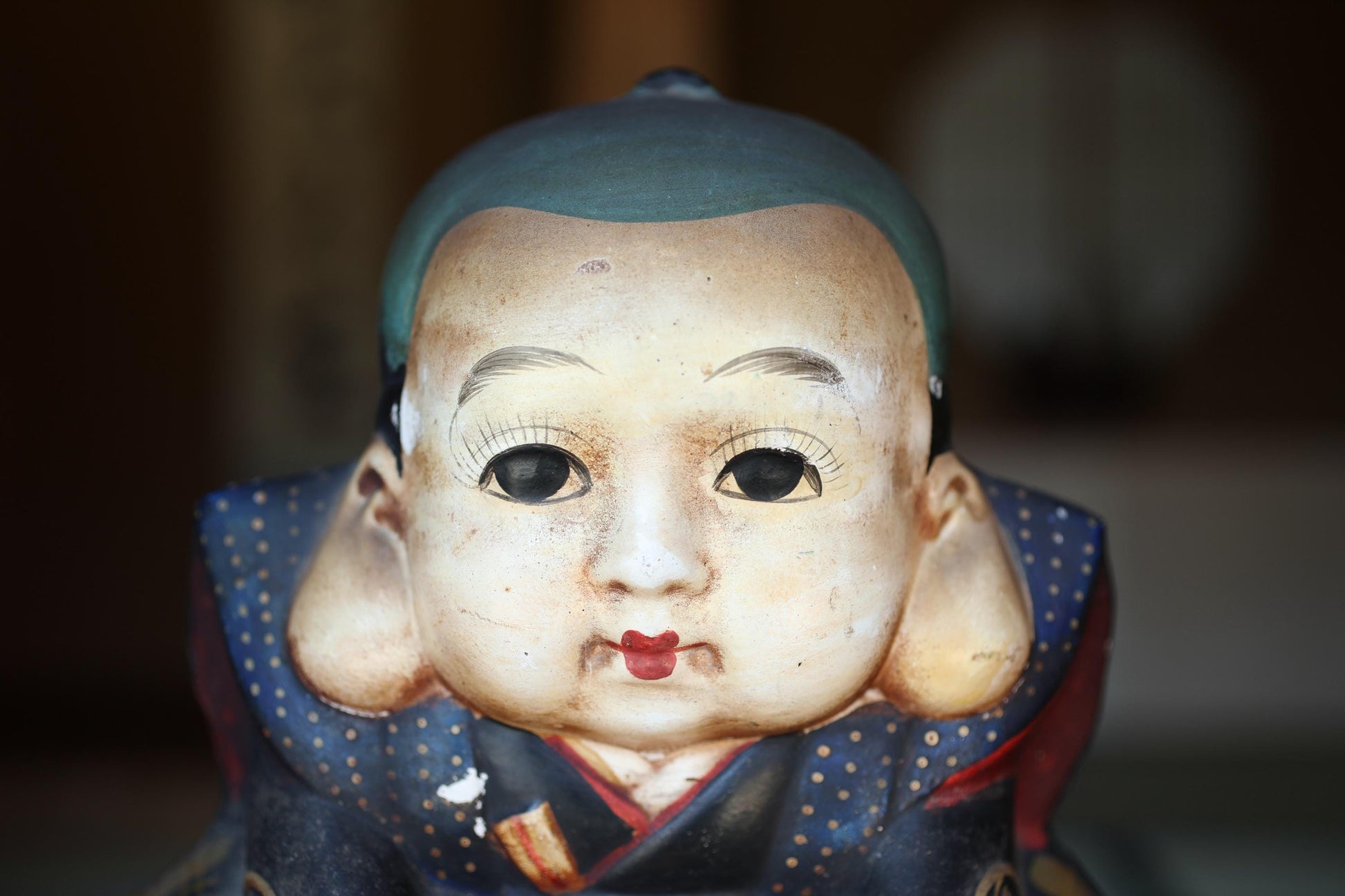 A close-up of a ceramic figurine depicting a baby's face with a blue hat and red lips.