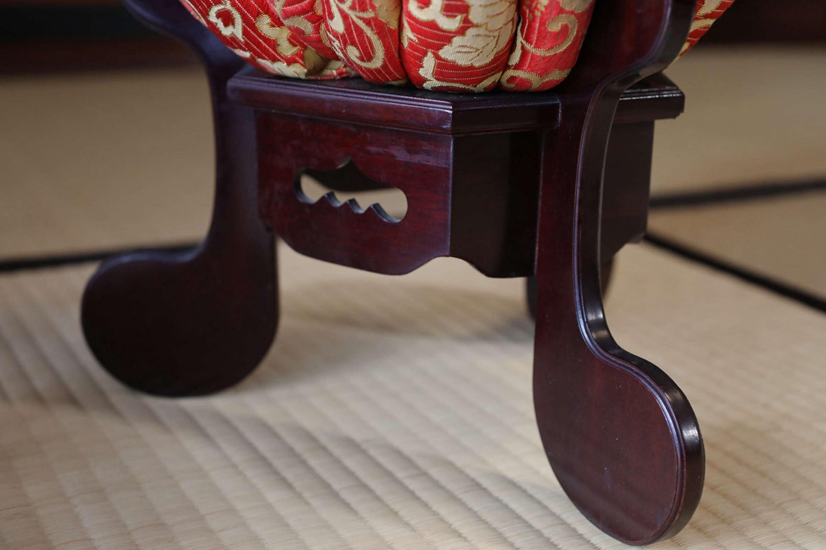 a close-up view of a dark wooden chair with a red and gold patterned cushion on the seat.
