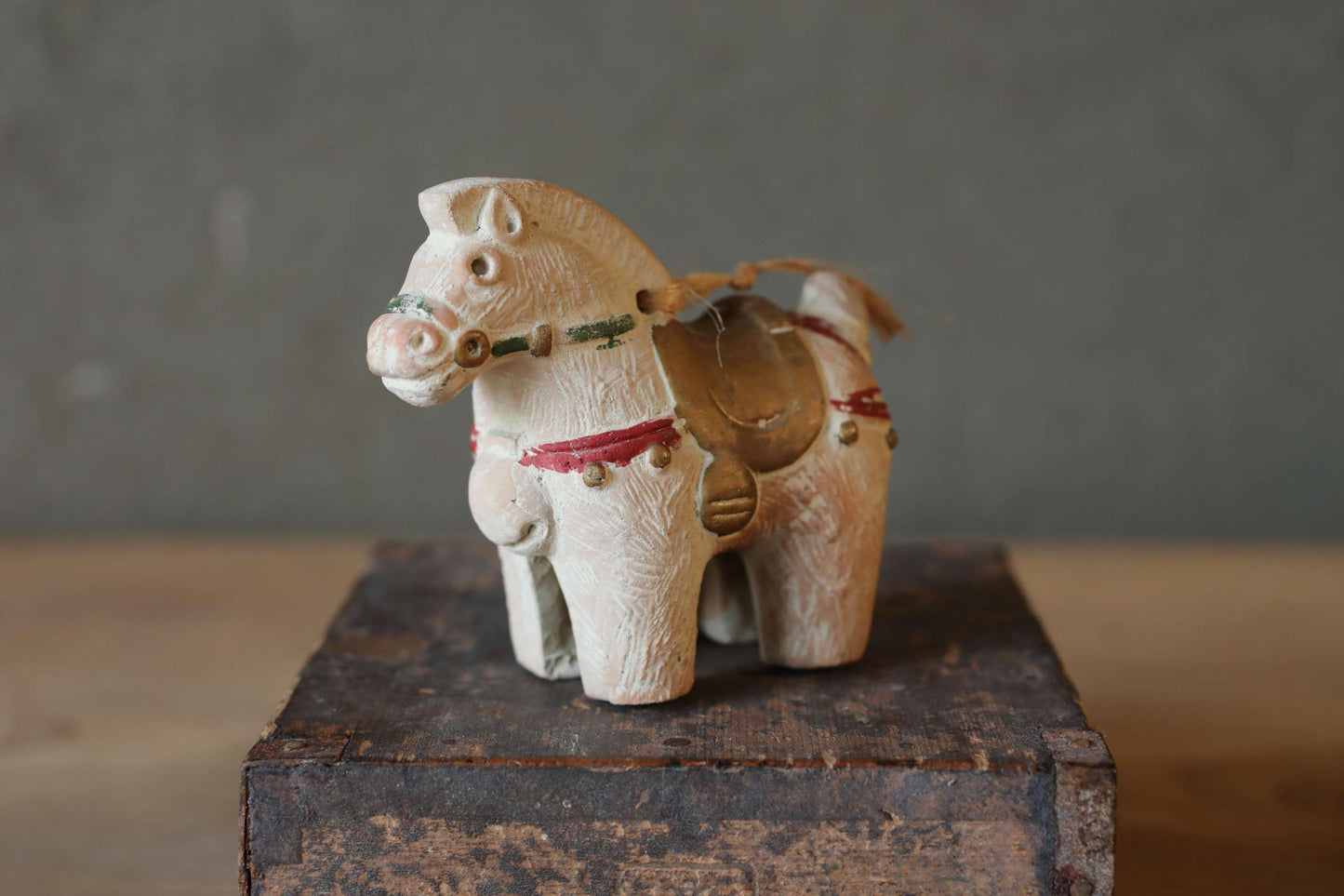 A small, white wooden figurine of a horse is sitting on a wooden surface.
