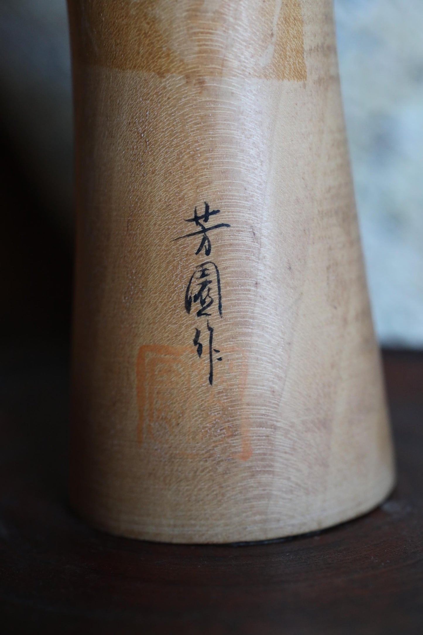 a close-up view of a wooden object, possibly a vase or a container, with a small black symbol or text inscribed on it.