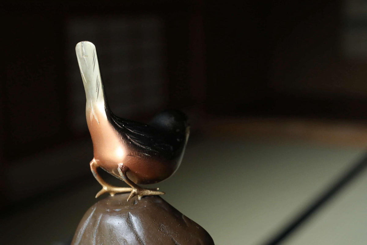 A small brown bird figurine perched on a brown rock.