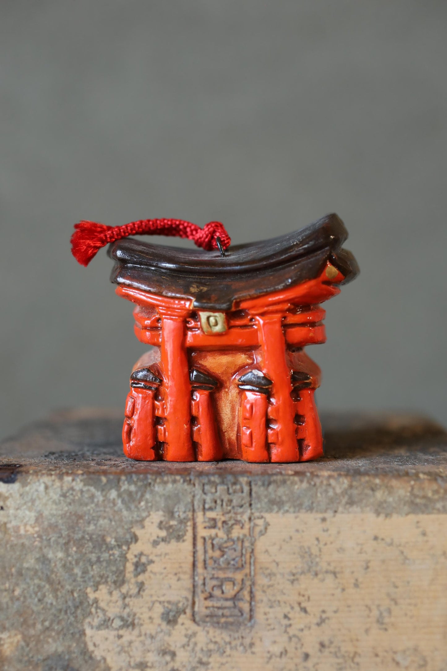 A small, red figurine with a black tassel attached to it, placed on a wooden surface.