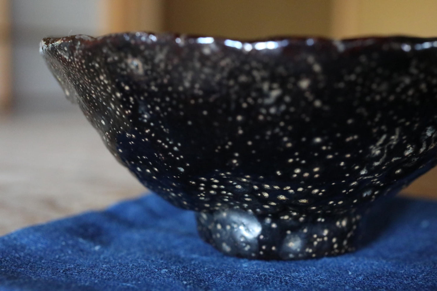 A close-up image of a black ceramic bowl with a speckled pattern, resting on a blue cloth.