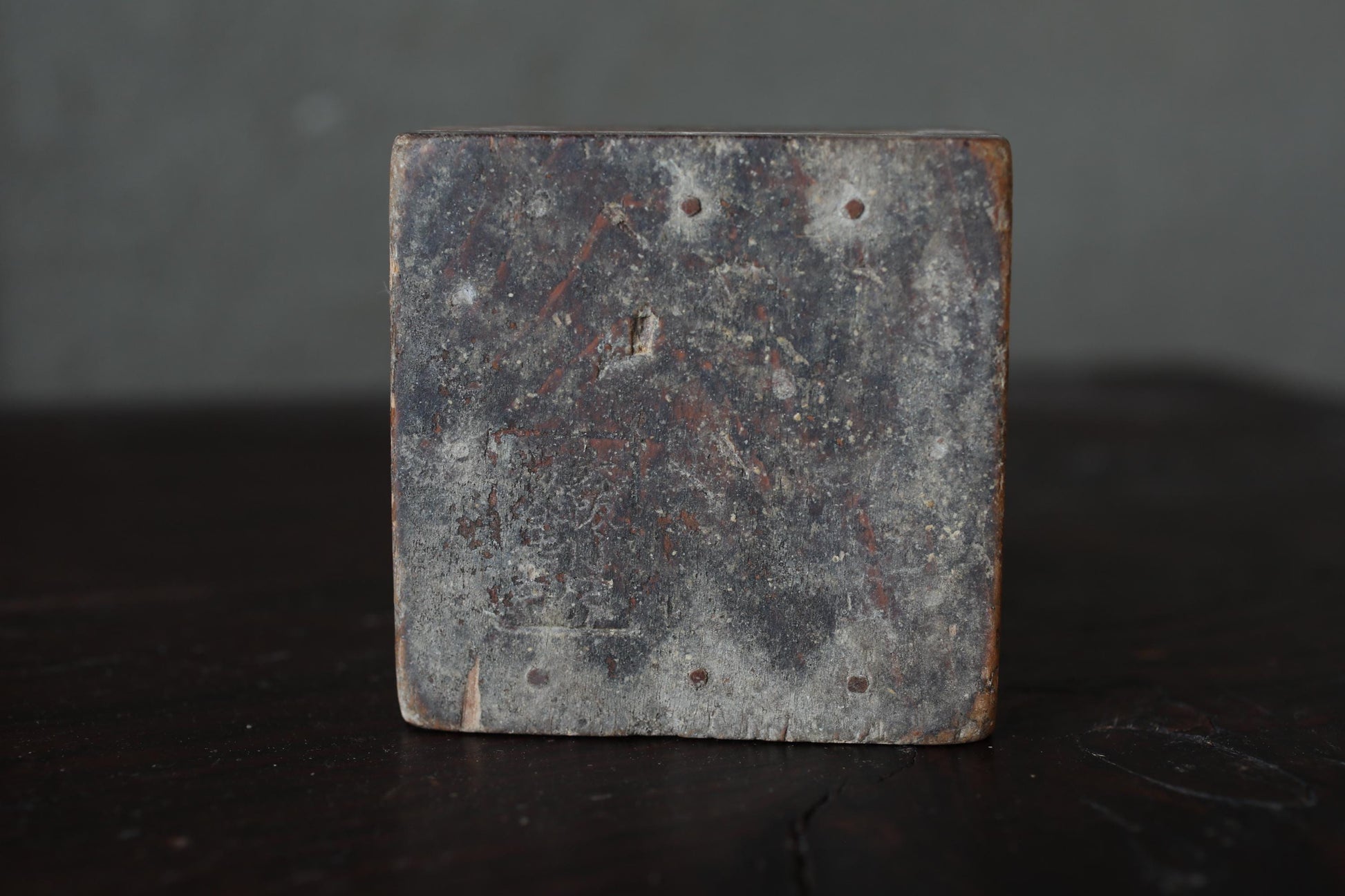 a square, weathered piece of metal or stone with a rough, textured surface.