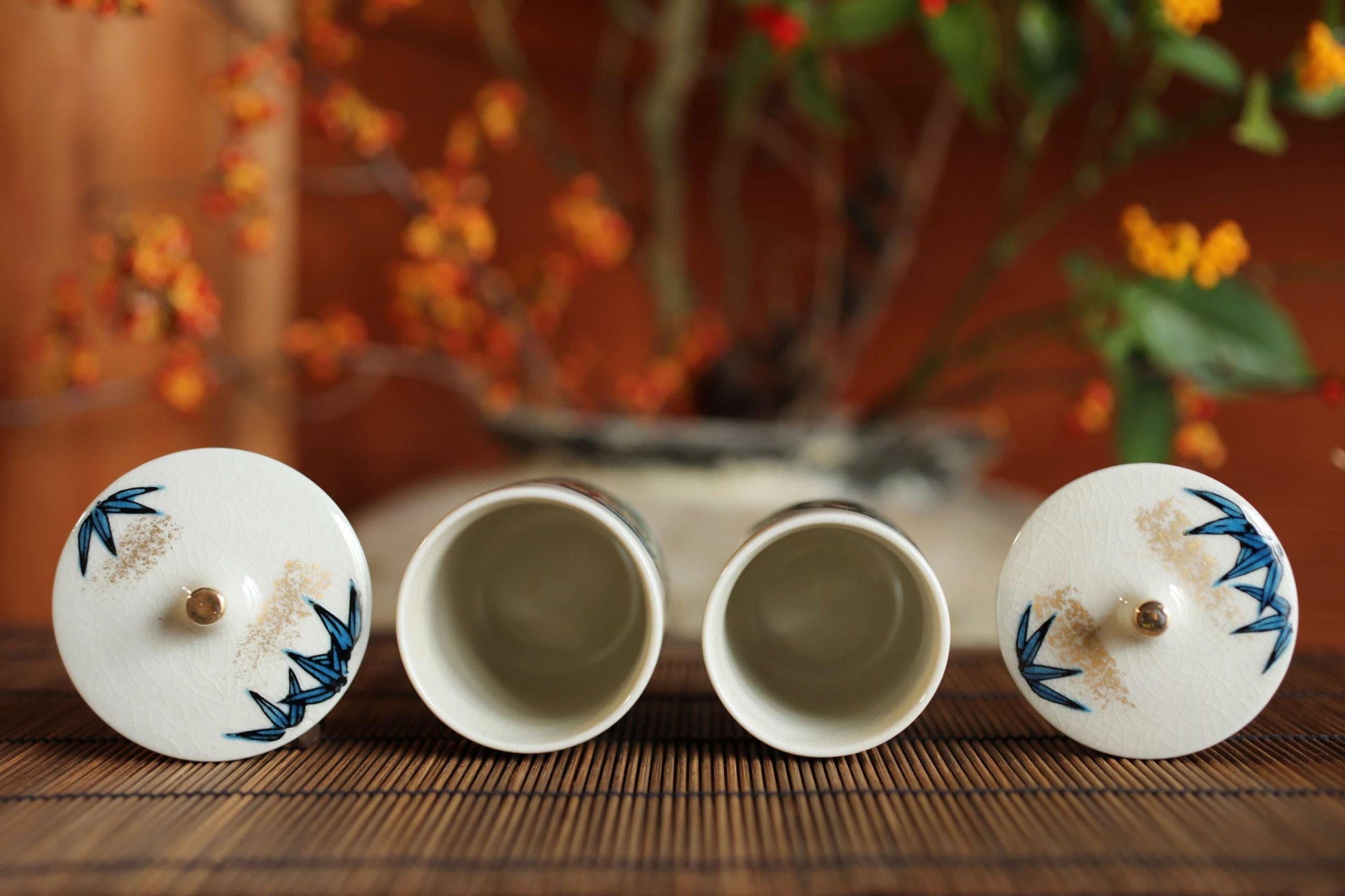 two white ceramic cups with blue floral designs on their lids, placed on a bamboo mat.