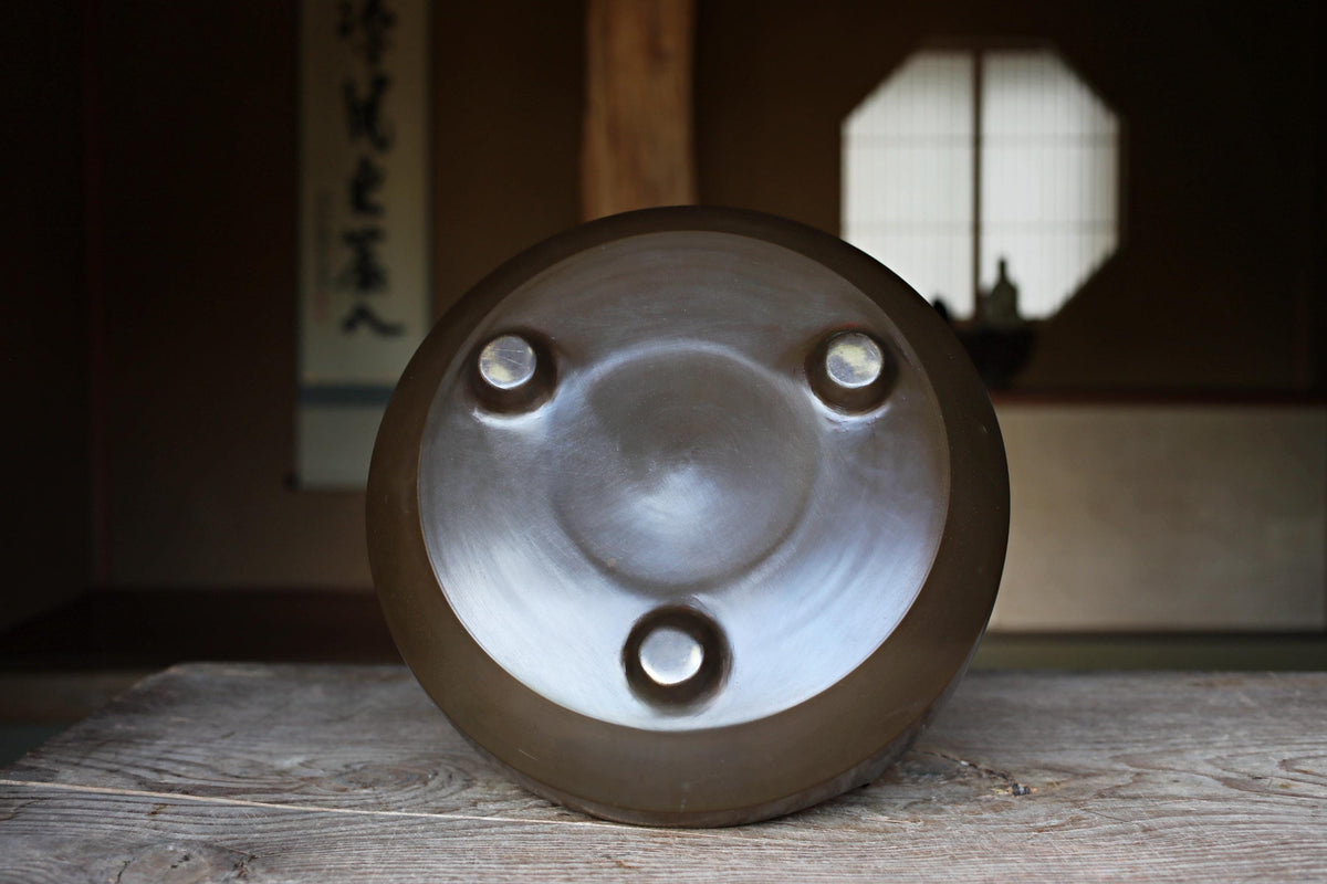 A ceramic bowl with three circular holes on its surface, placed on a wooden surface.