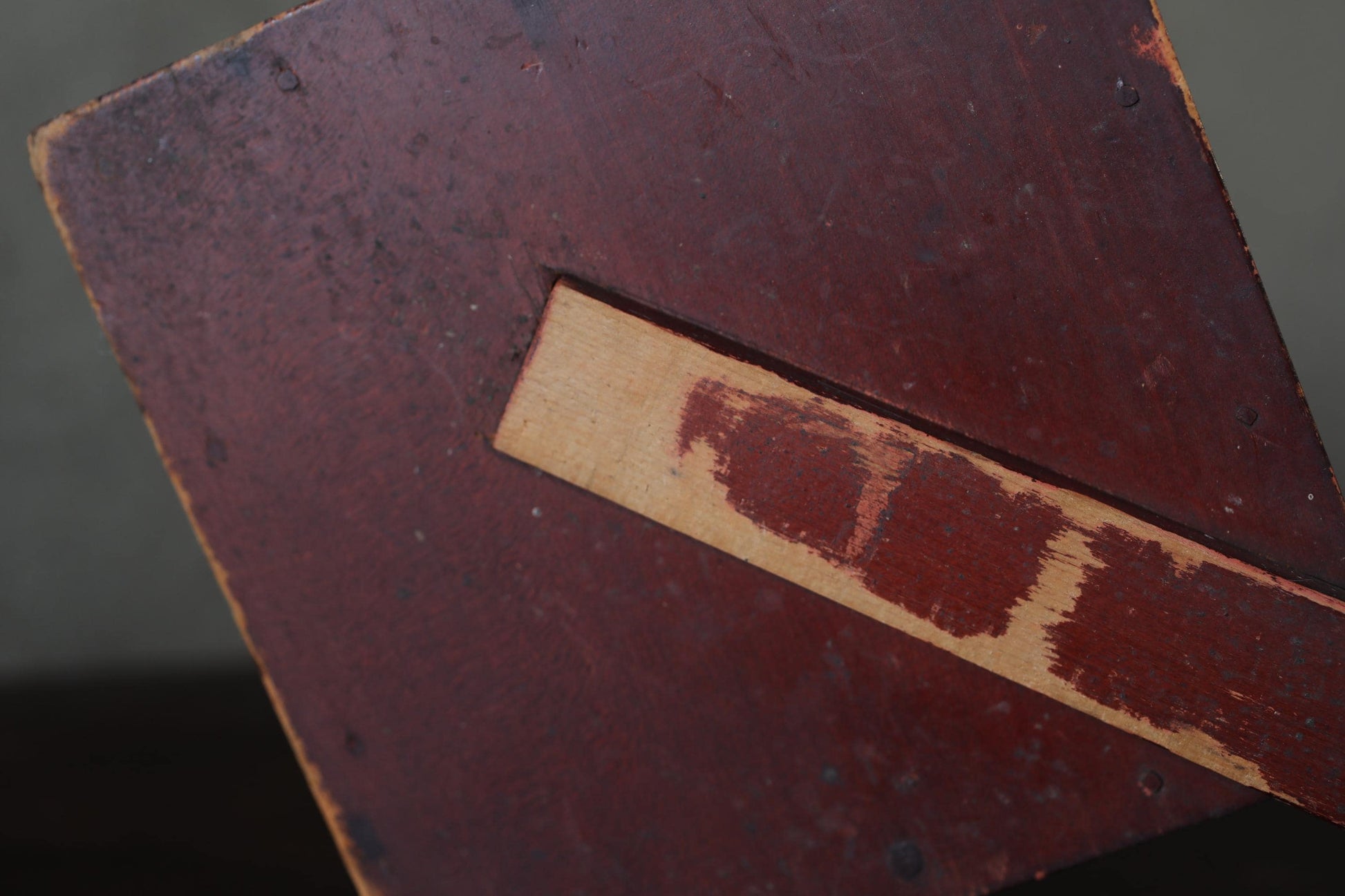 a close-up view of a wooden surface with a red-brown color and a visible grain pattern.