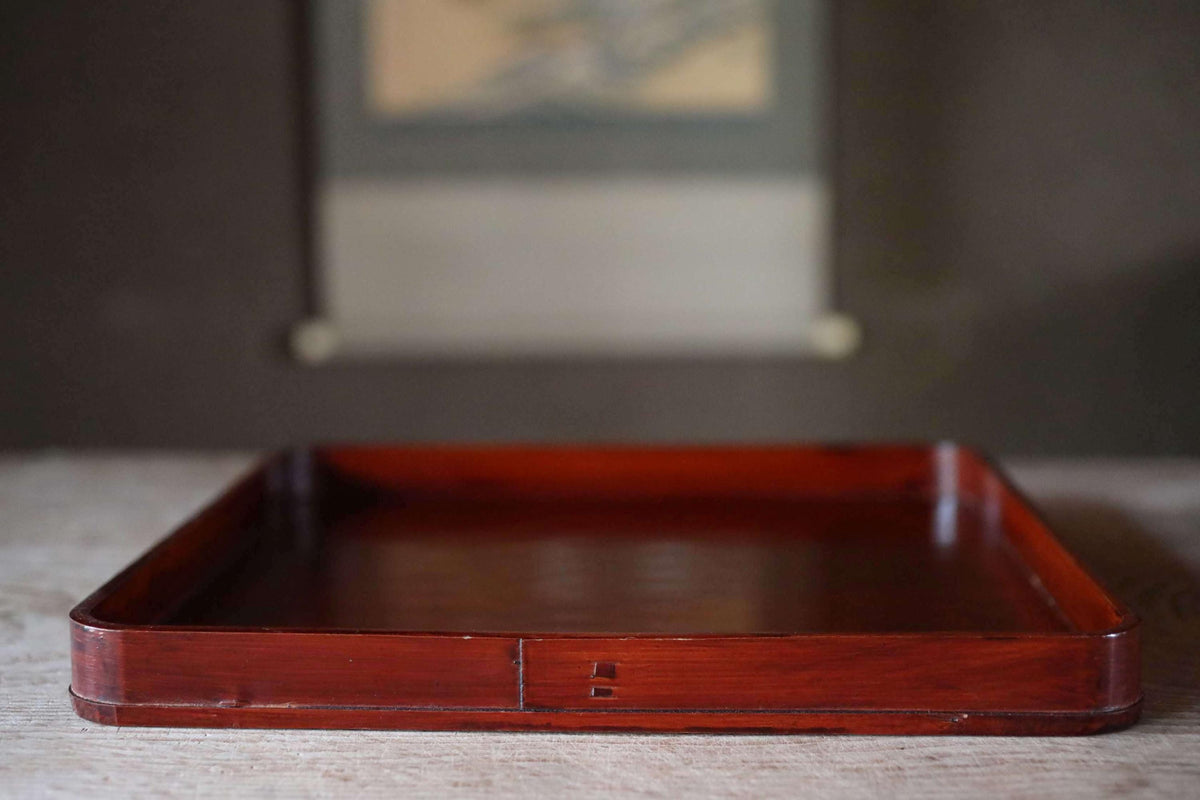 A wooden tray with a dark finish sits on a wooden surface.