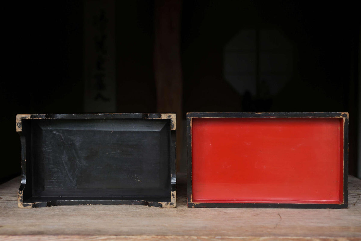 Two wooden boxes, one black and one red, are placed side by side on a wooden surface.