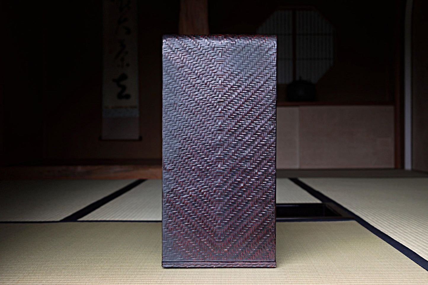 a dark brown woven object, possibly a piece of furniture or a decorative item, placed on a tatami mat in a dimly lit room.