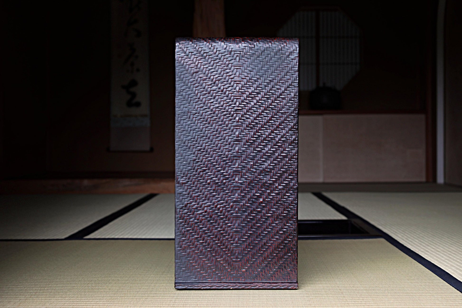 a dark brown woven object, possibly a piece of furniture or a decorative item, placed on a tatami mat in a dimly lit room.