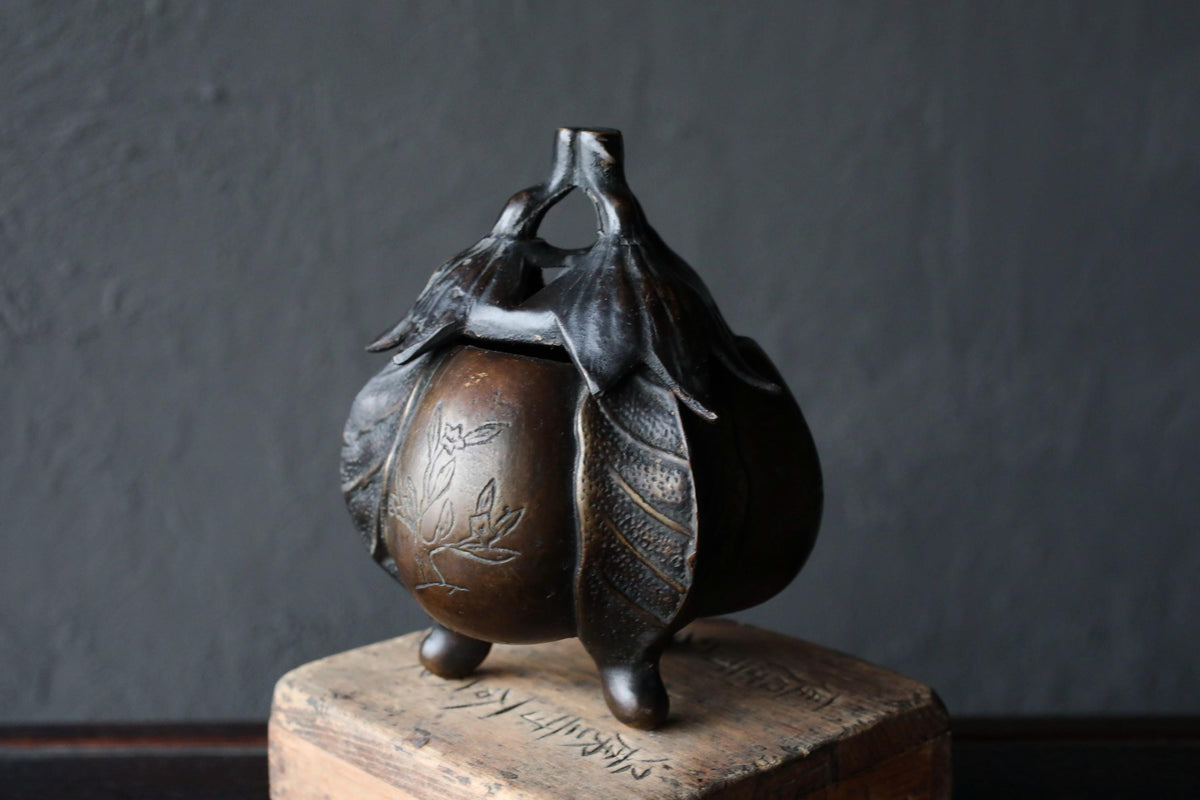 A bronze incense burner with a floral design on its surface, placed on a wooden base.