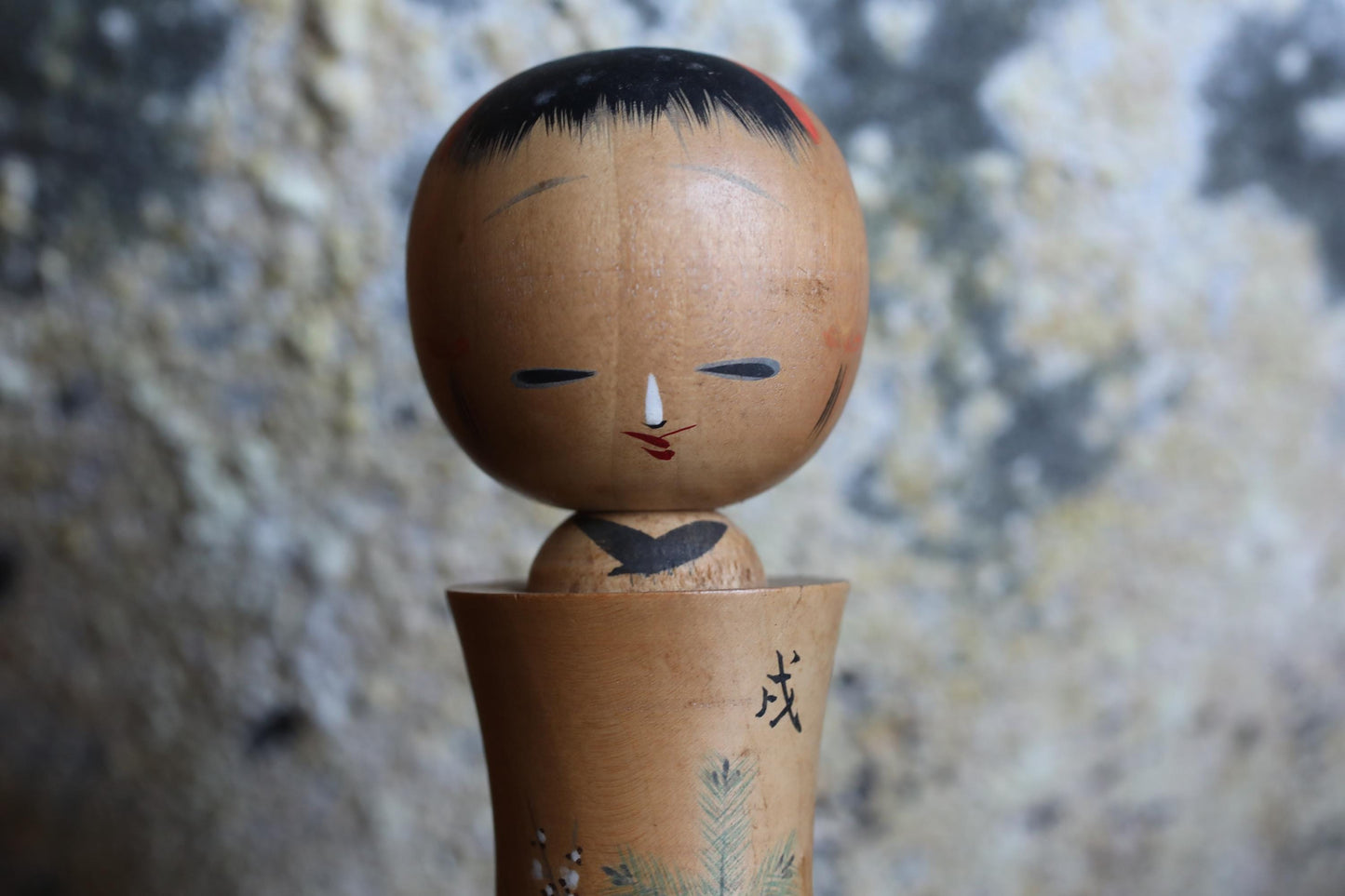 A wooden doll with a face and a small body, standing on a wooden base with some decorative elements.