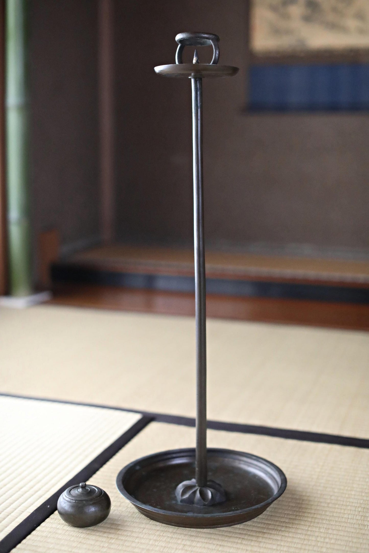 a tall, black metal candle holder with a round base and a small, round metal object placed on the floor next to it.