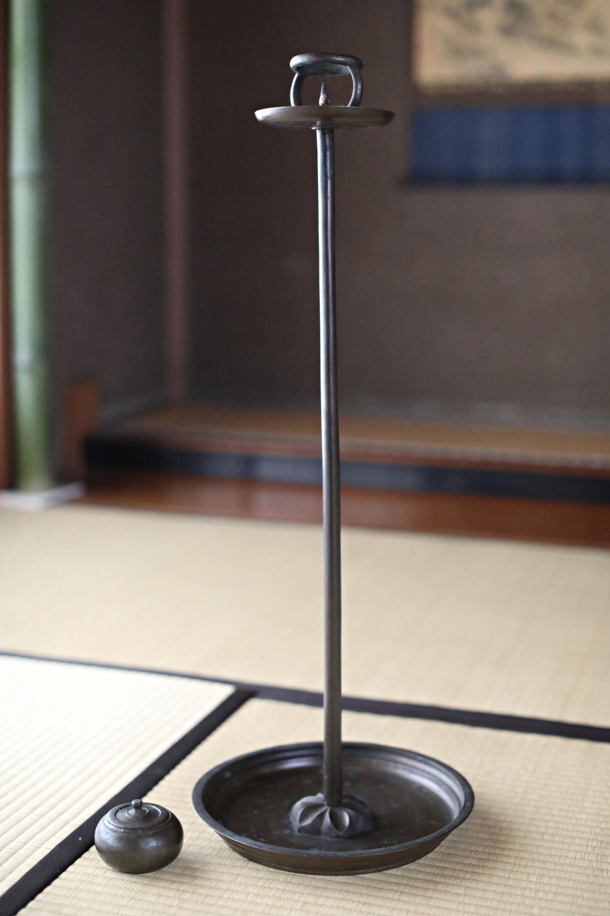 a tall, black metal candle holder with a round base and a small, round metal object placed on the floor next to it.