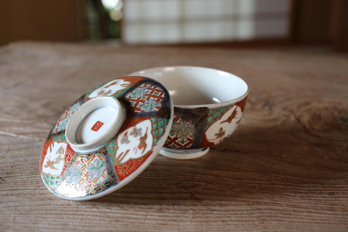 A colorful ceramic bowl with intricate patterns rests on a wooden surface, with the lid of the bowl visible.