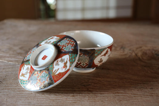 A colorful ceramic bowl with intricate patterns rests on a wooden surface, with the lid of the bowl visible.