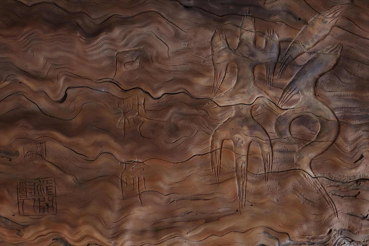 The image is a close-up of a textured surface with various carved patterns and designs, including abstract shapes and symbols.
