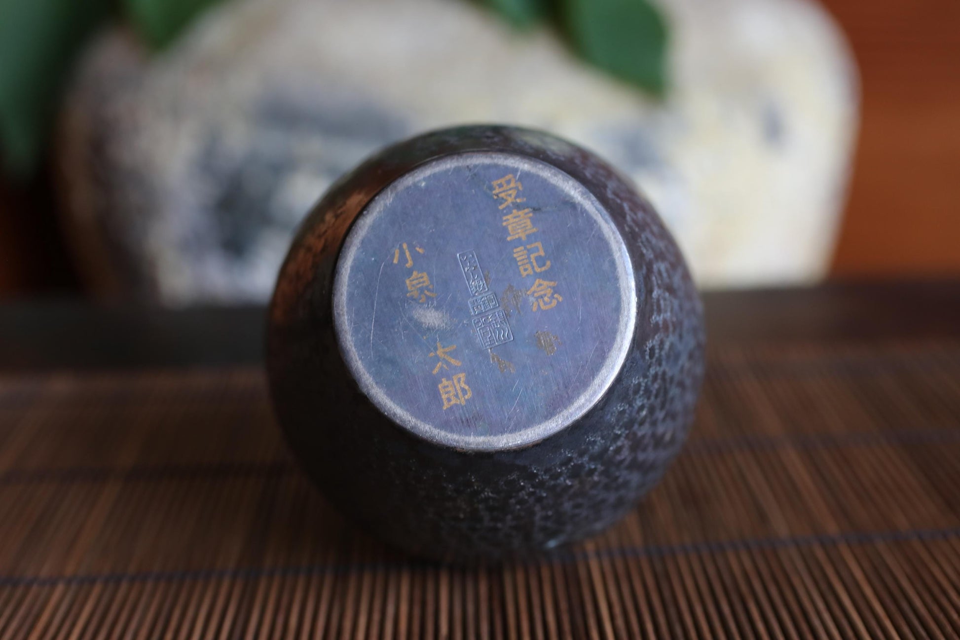 A close-up image of a dark-colored vase or container with Chinese characters on its surface, placed on a wooden surface.