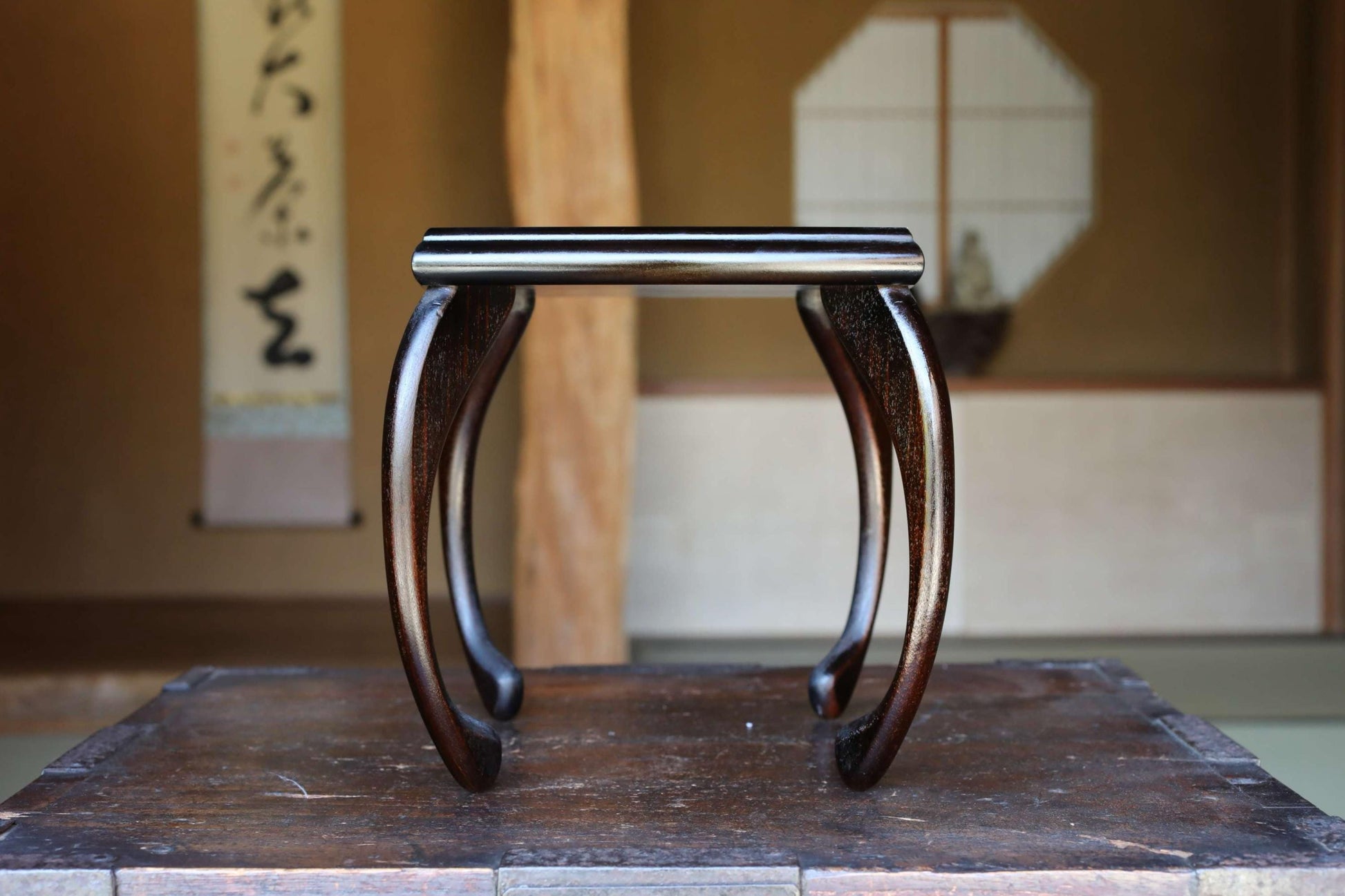 A dark wooden table with a curved top, placed in a room with a traditional Japanese-style wall and a sliding door.