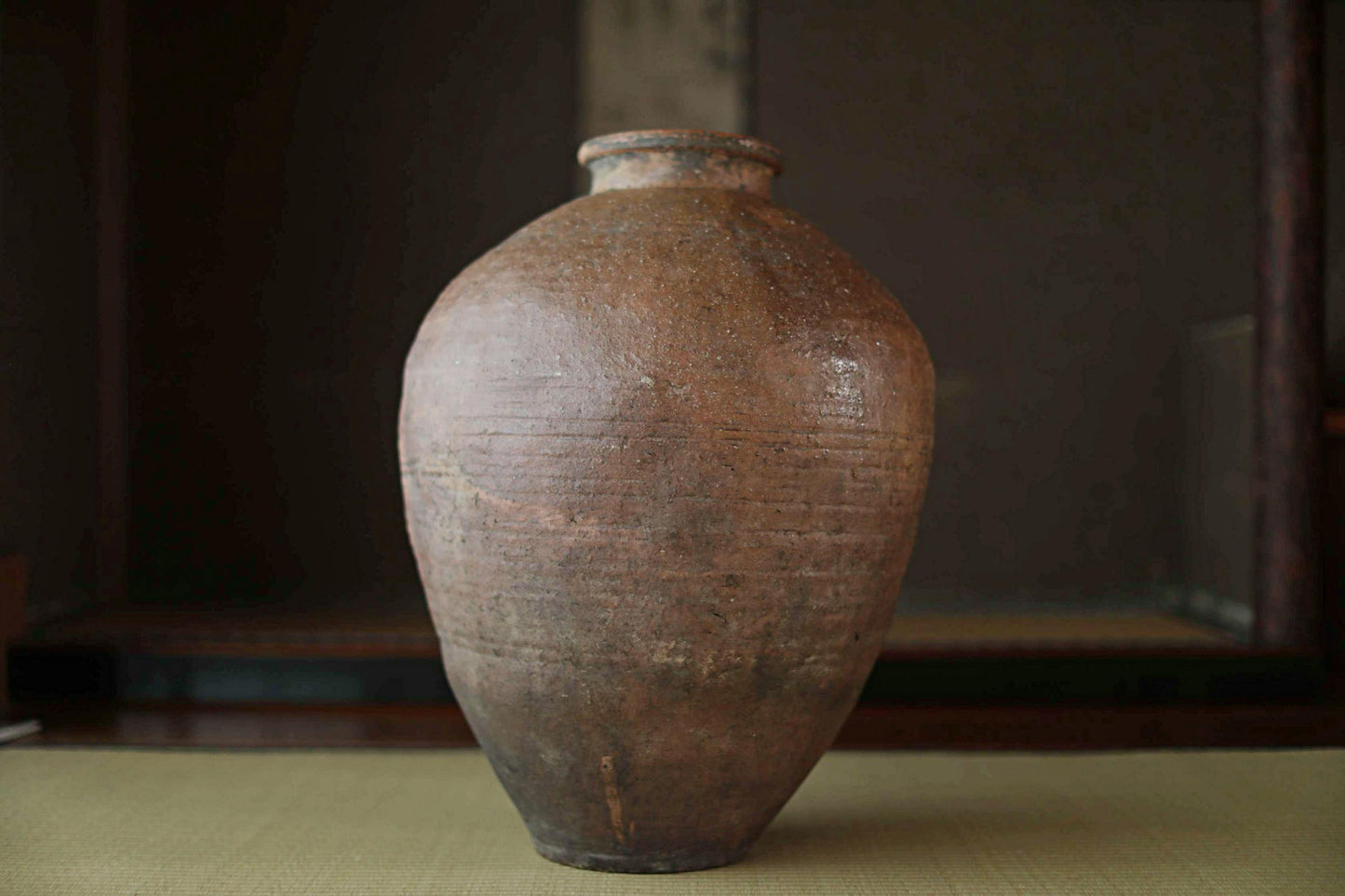 An old, weathered clay vase with a round shape and a small opening at the top, sitting on a surface.
