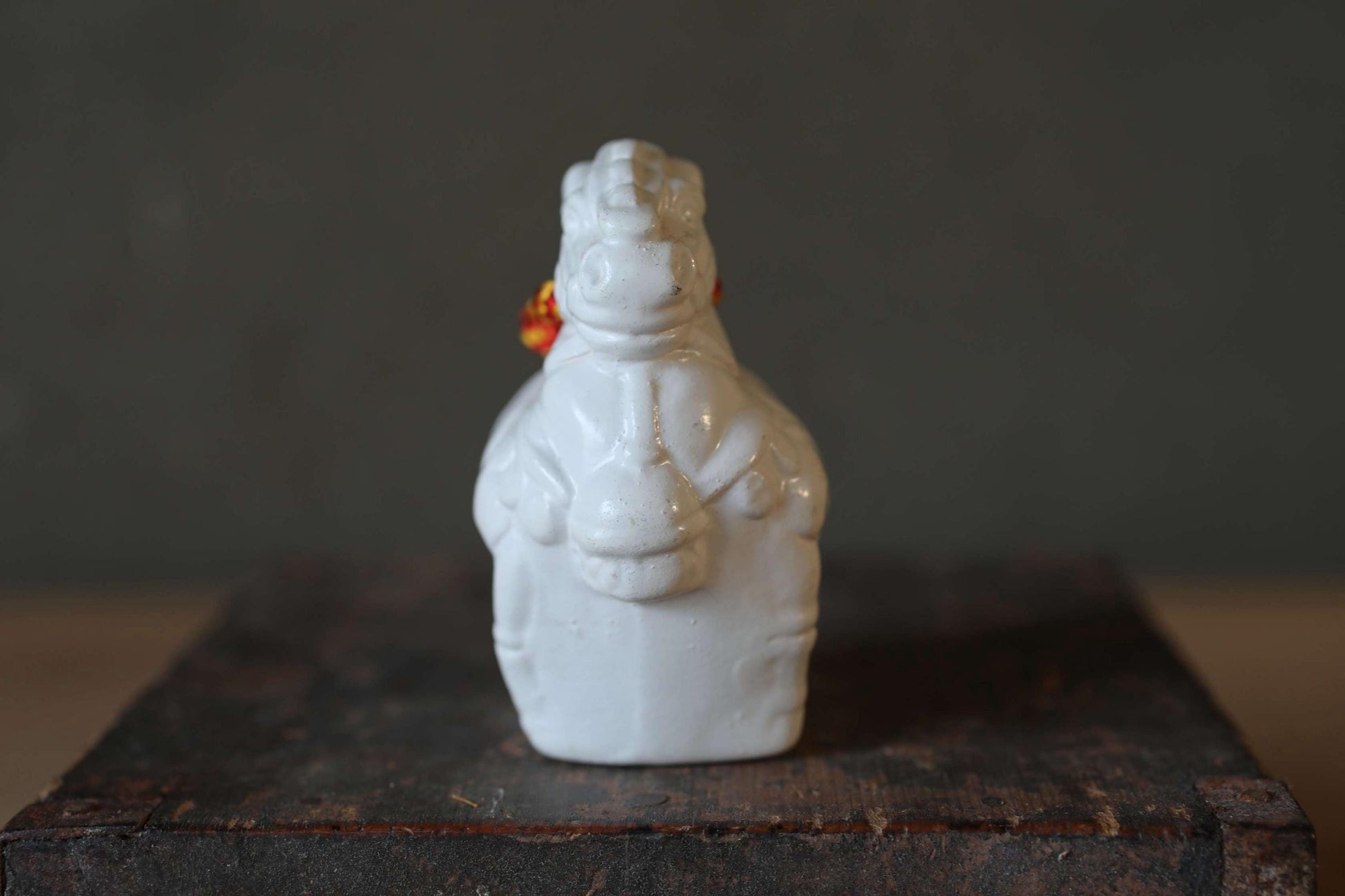 A white ceramic figurine of a horse, with a red ribbon around its neck, is sitting on a wooden surface.