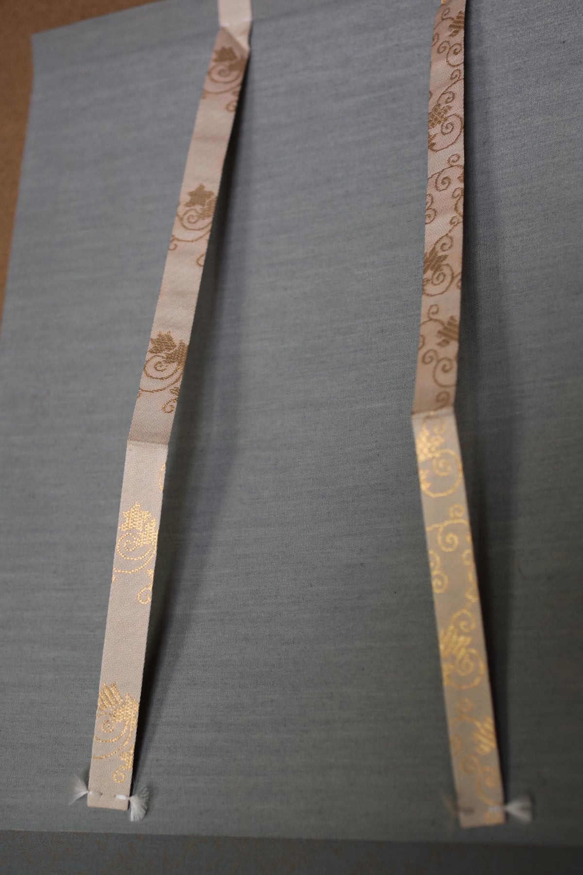 two decorative ribbons with a floral pattern, attached to a gray surface.