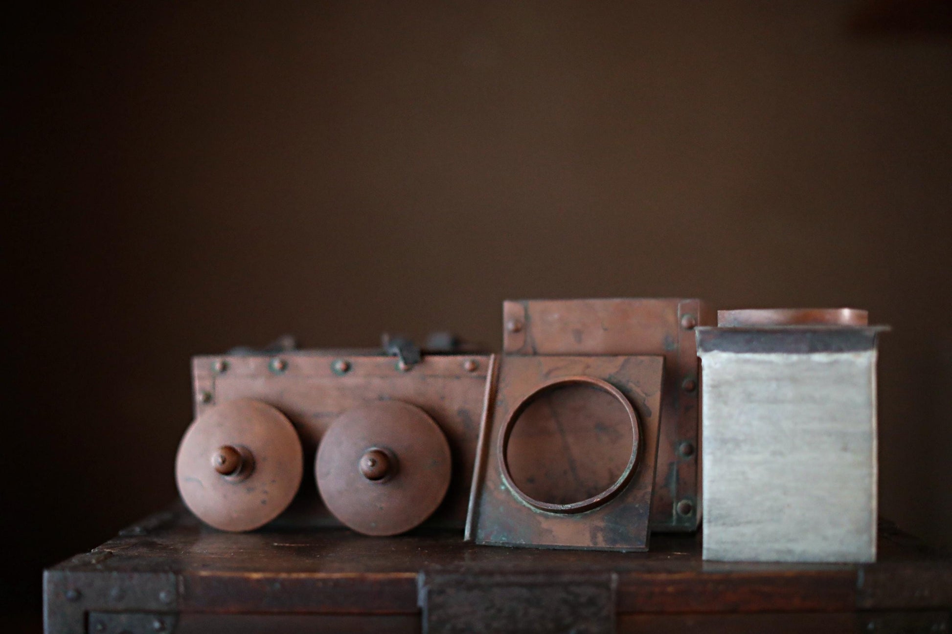 a collection of antique metal objects, including a large metal box, a metal cylinder, and a metal plate, arranged on a wooden surface.
