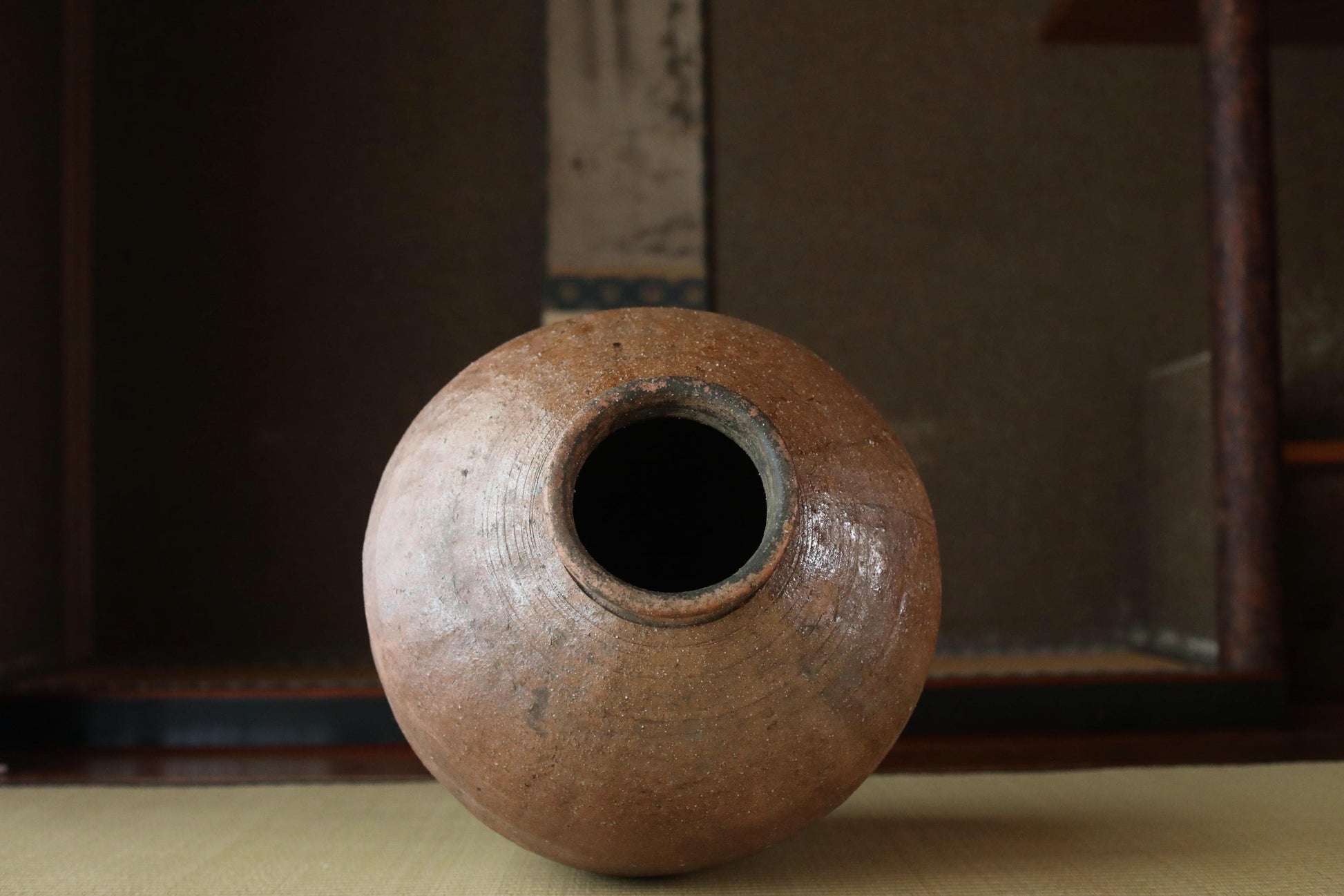 An old, round clay vase with a large hole in the center, sitting on a wooden surface.