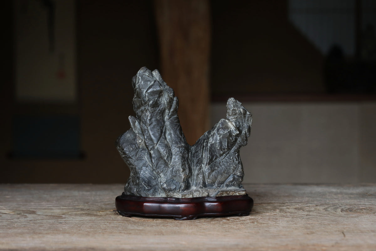A gray stone sculpture is displayed on a wooden stand on a wooden surface.