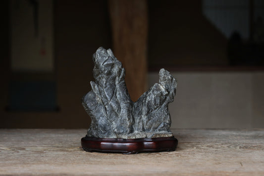 A gray stone sculpture is displayed on a wooden stand on a wooden surface.