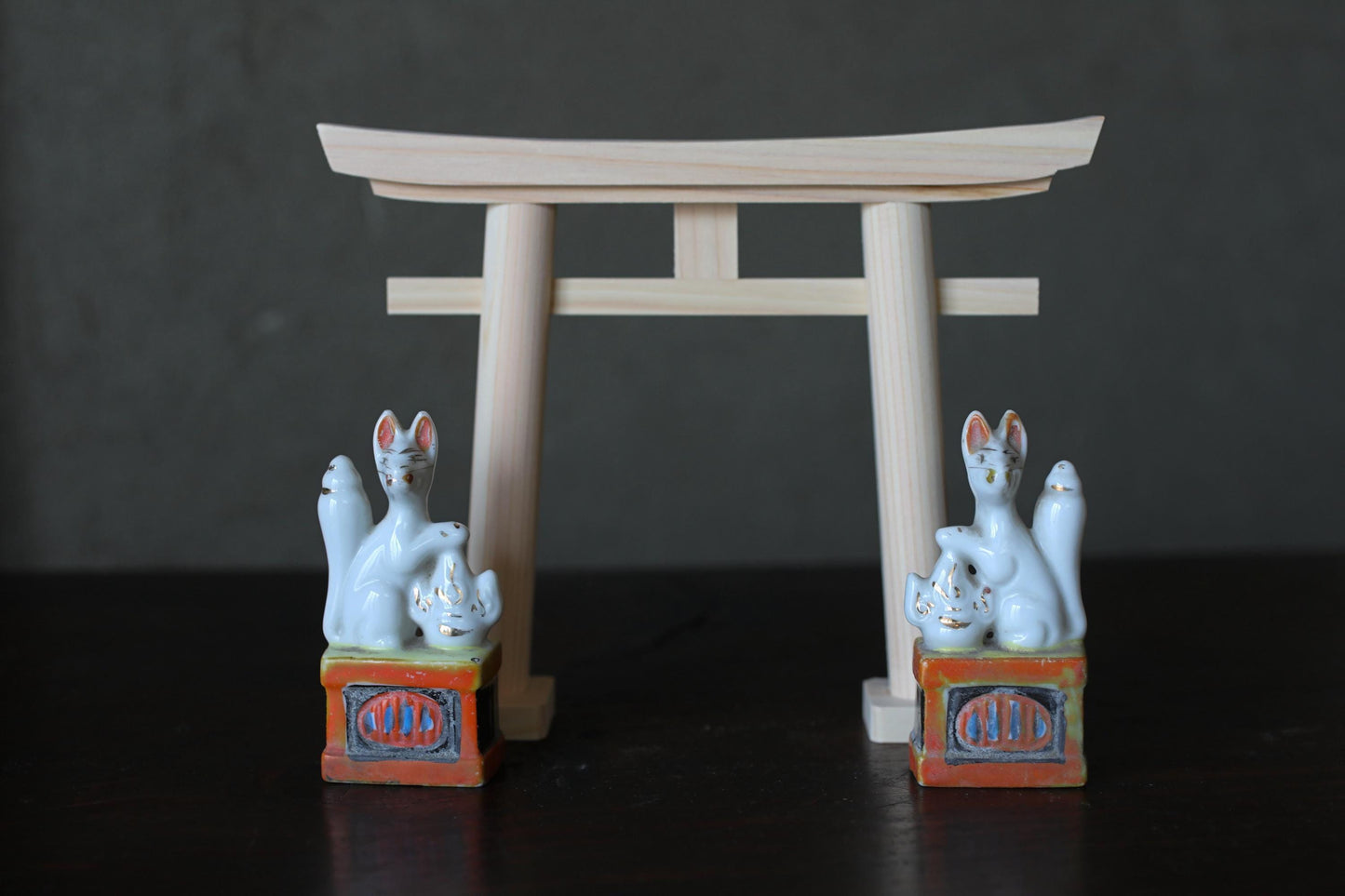 two ceramic fox statues positioned on either side of a wooden torii gate, which is a traditional Japanese gate used at shrines and other sacred sites.