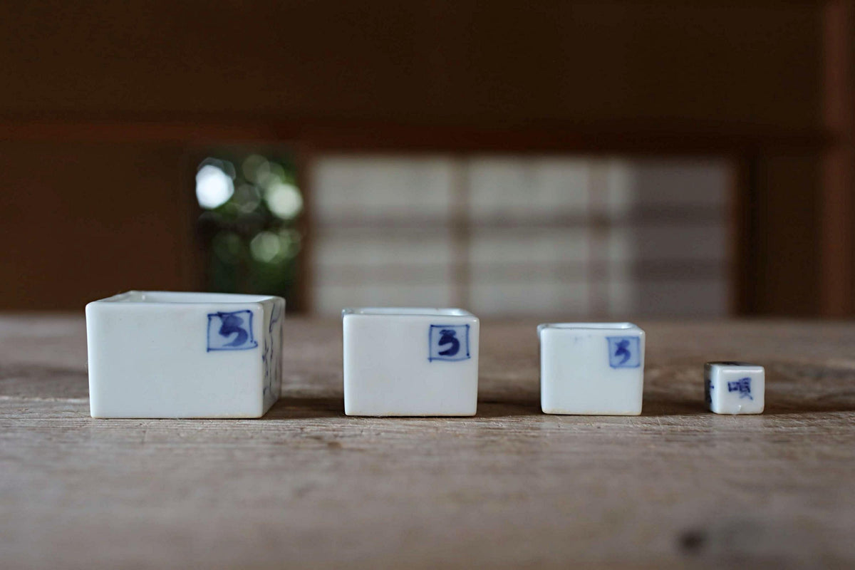 Three white ceramic containers with blue markings are arranged in a row on a wooden surface.