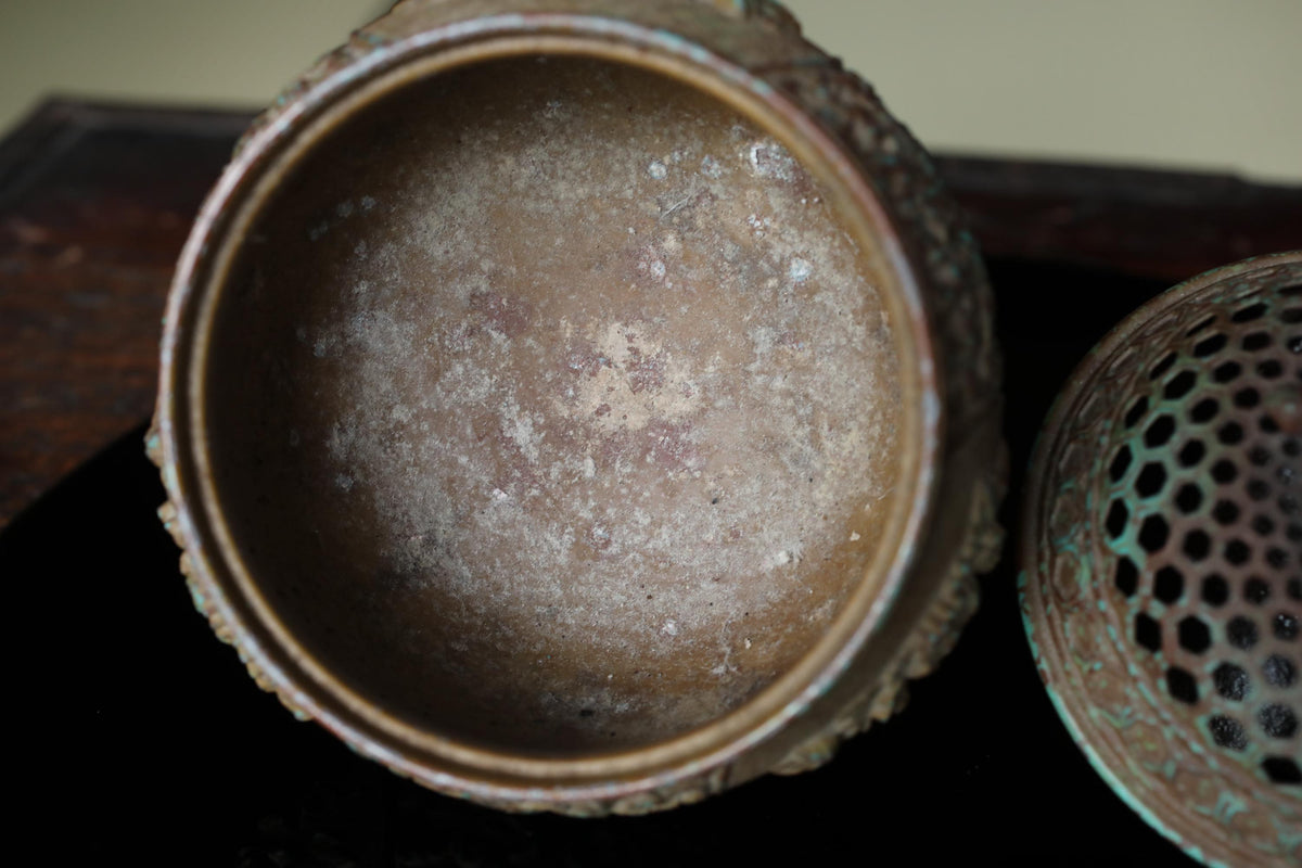 an old, rusted metal container with a hole in the lid, sitting on a dark surface.