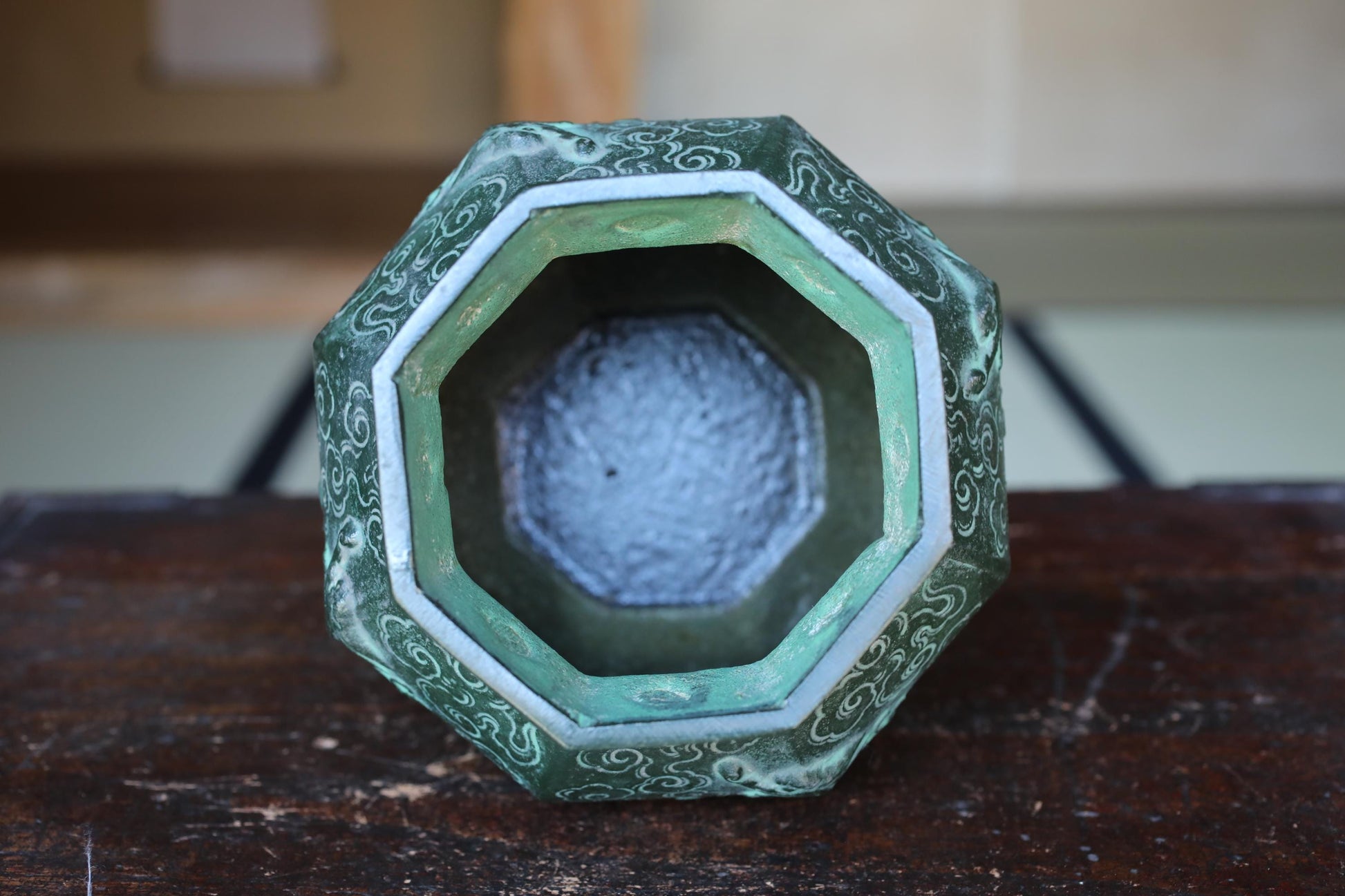 a green and white ornate vase or container with a patterned design, sitting on a wooden surface.