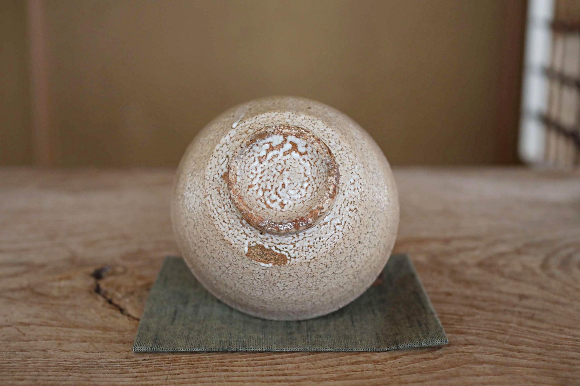 A white ceramic bowl with a speckled texture sits on a green cloth on a wooden surface.
