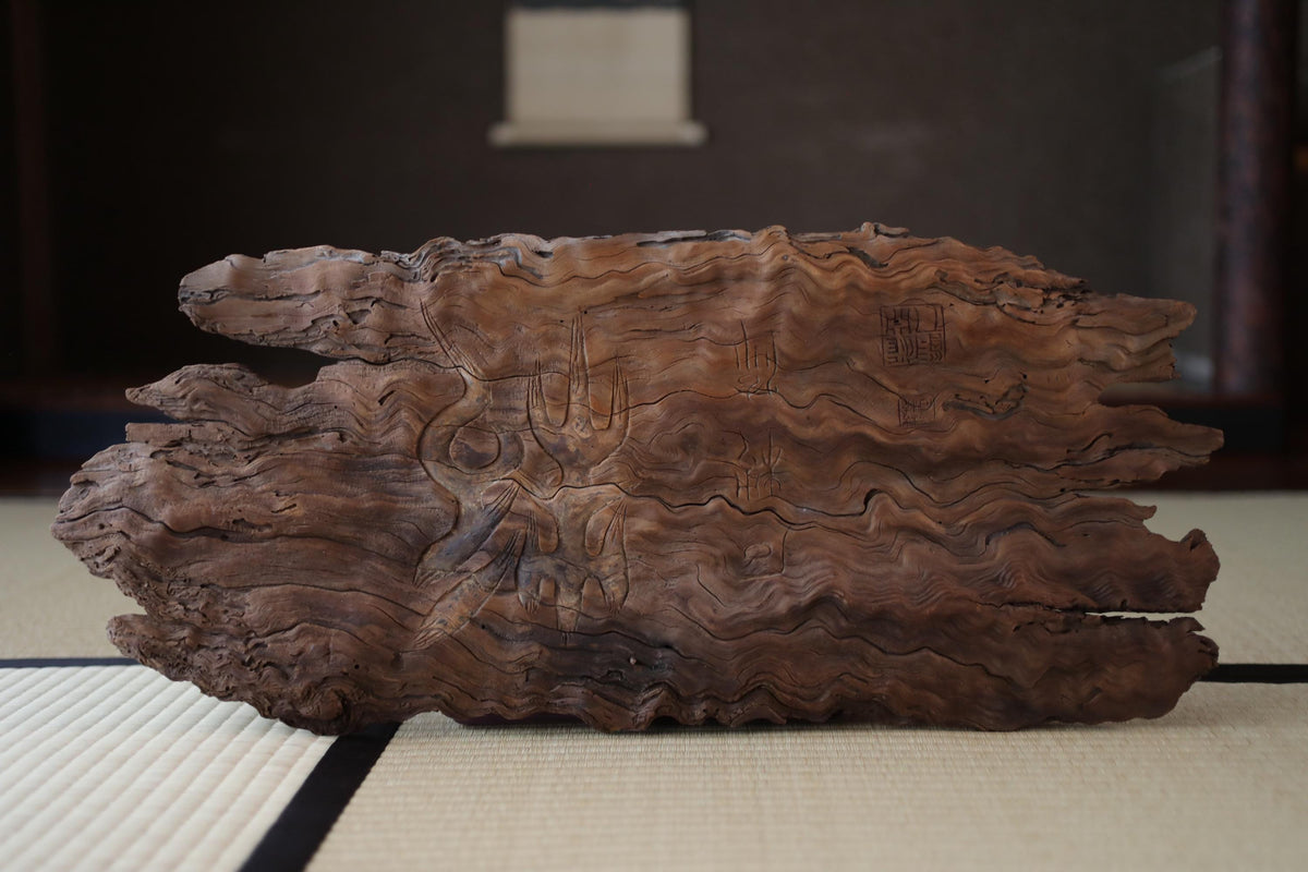 a large, weathered piece of wood with a distinctive wave-like pattern, sitting on a white mat.