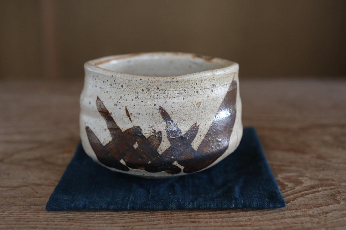 A ceramic bowl with a white and brown design sits on a blue cloth on a wooden surface.