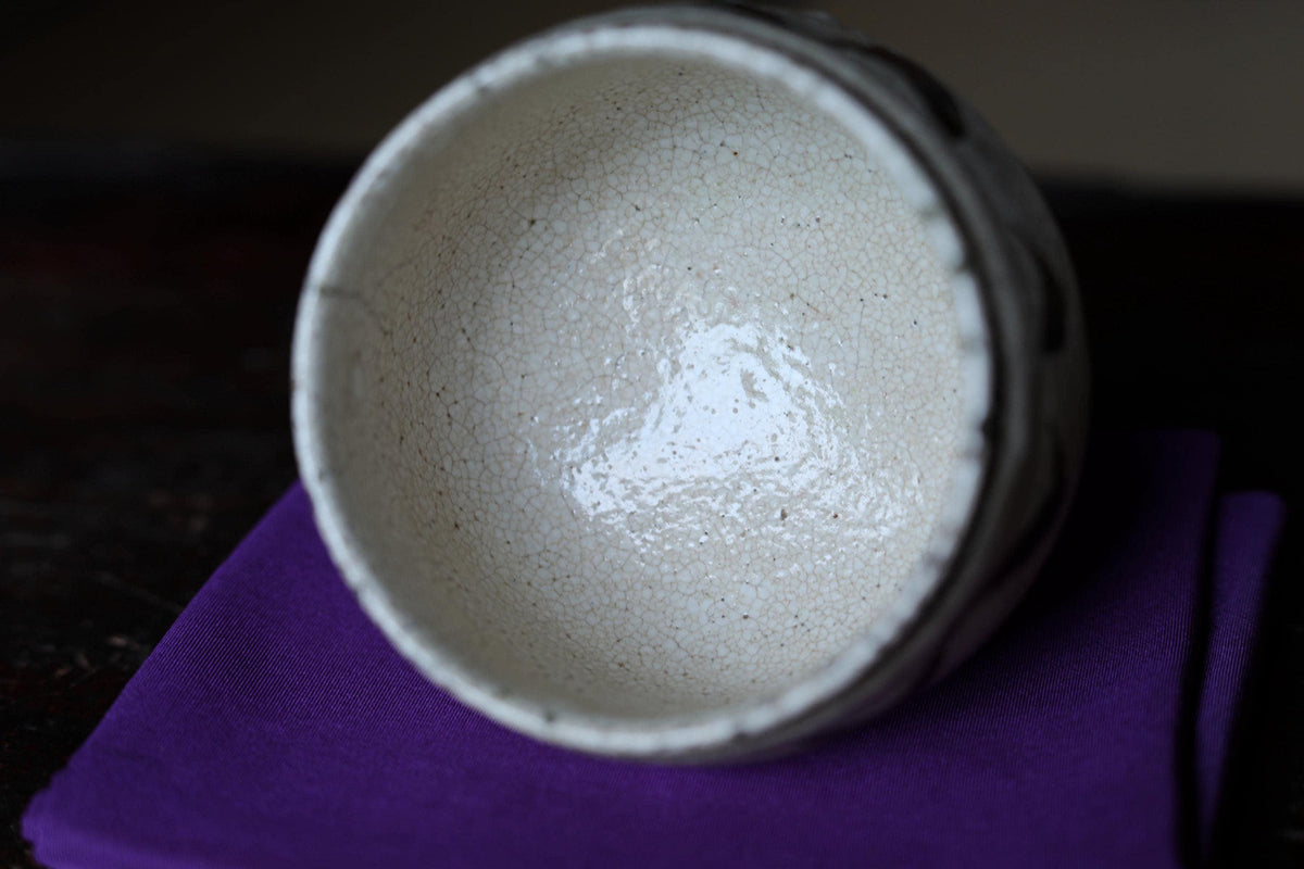 A white ceramic bowl with a textured surface sits on a purple cloth.