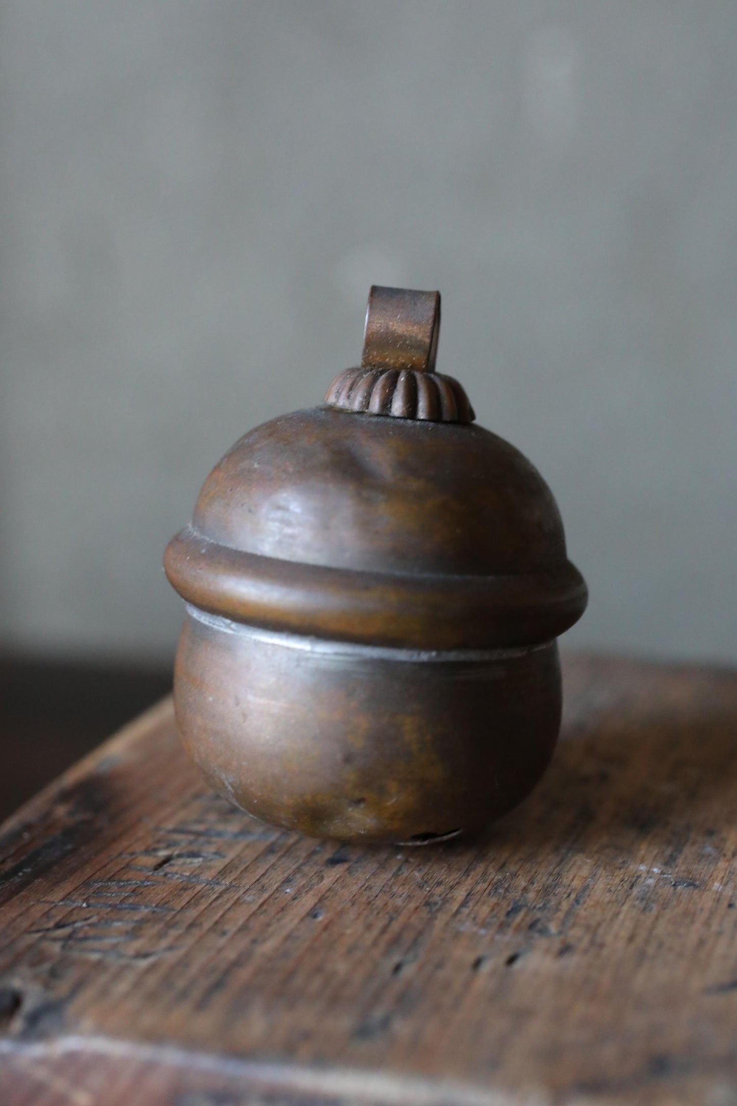 A round, metal bell-shaped container with a small finial on top, sitting on a wooden surface.